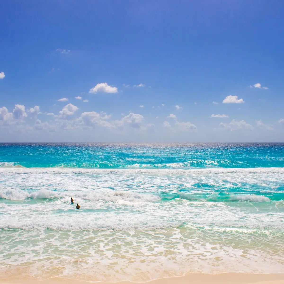 Mar azul-turquesa com ondas chegando na areia branca, em Cancún